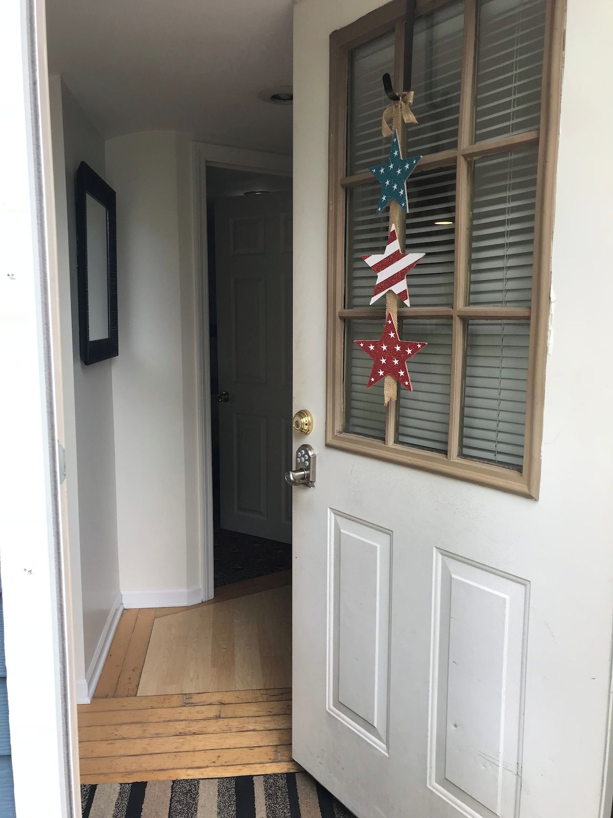 Une porte avec une fenêtre, un paillasson et un miroir fixé au mur.
