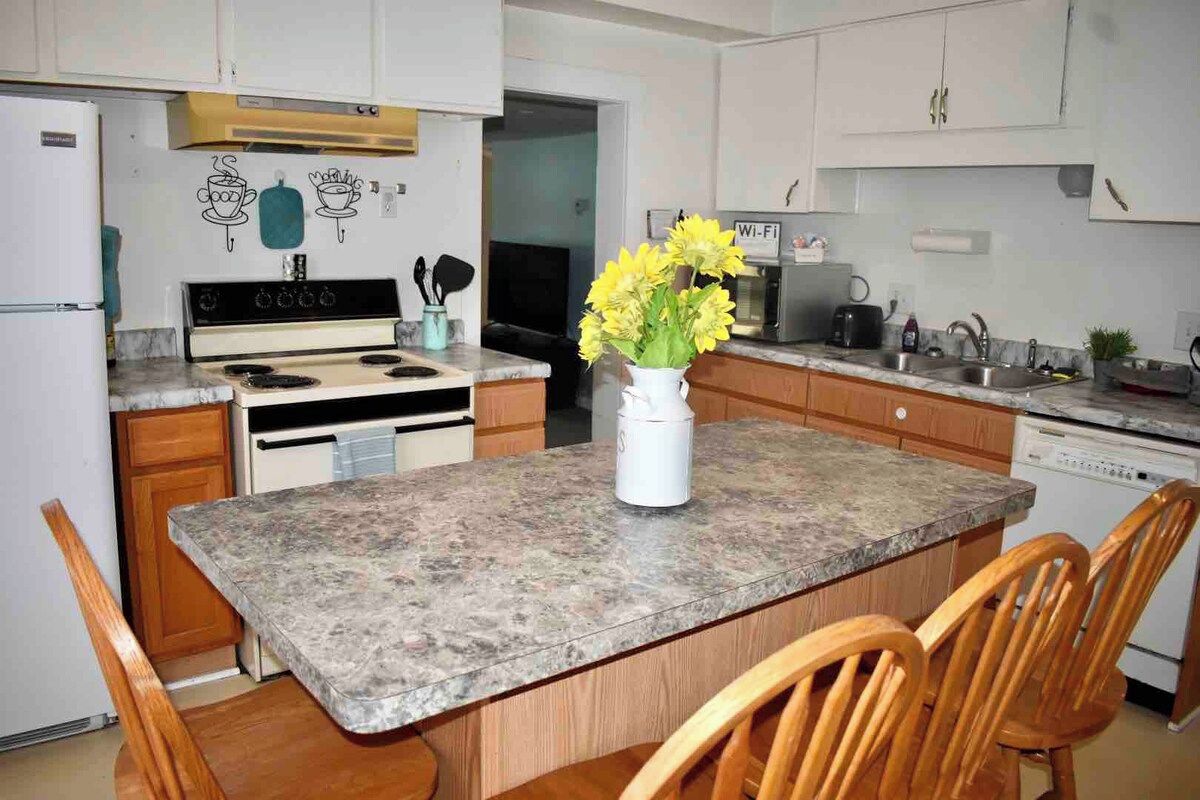 A kitchen with a granite countertop, wooden cabinets, a stove, and a dining area with chairs.