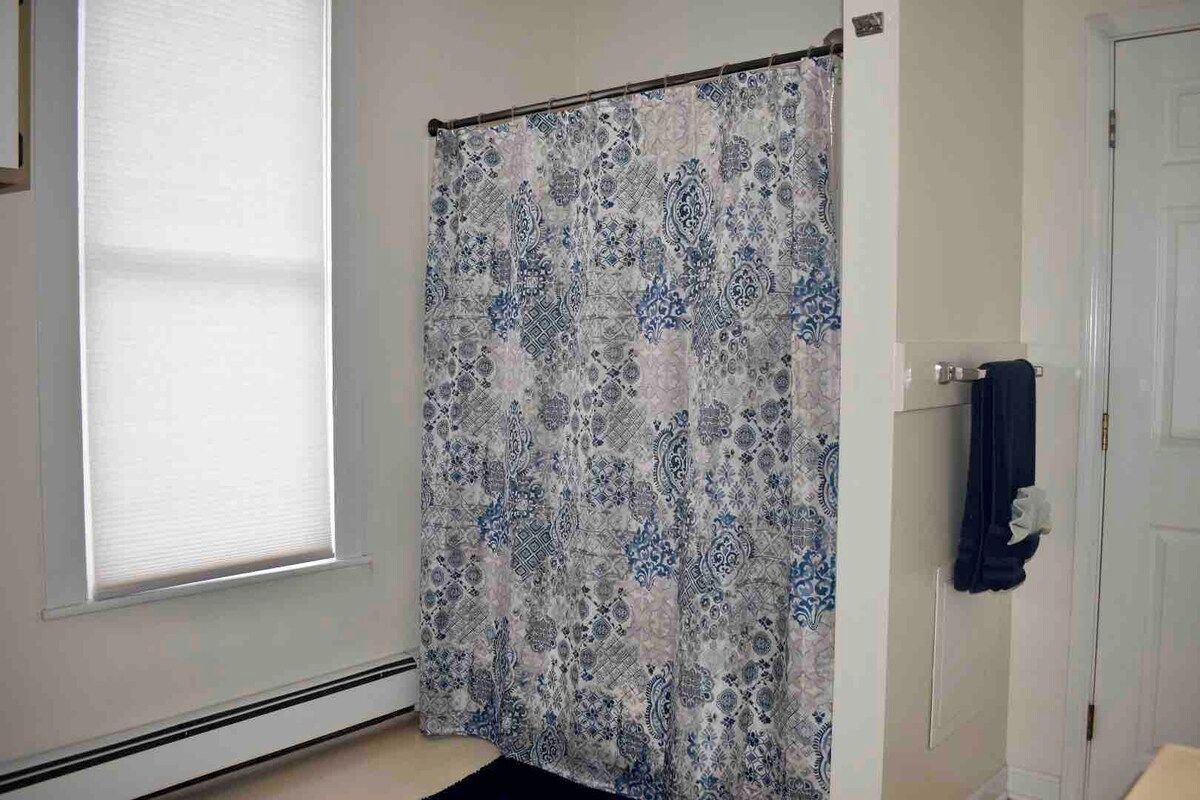 Un bagno con tenda doccia, asciugamano e finestra con persiane.