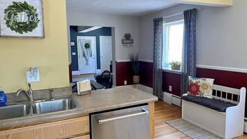 A compact kitchen with a built-in dishwasher, wooden cabinets, and a bench with decorative pillows.