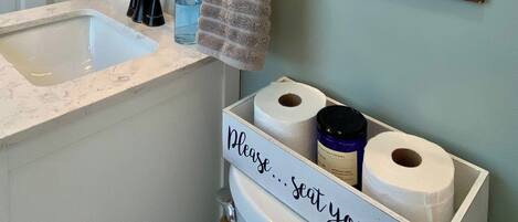 A bathroom with a sink, mirror, towel rack, and a sign that says 'TAKE A SEAT'.