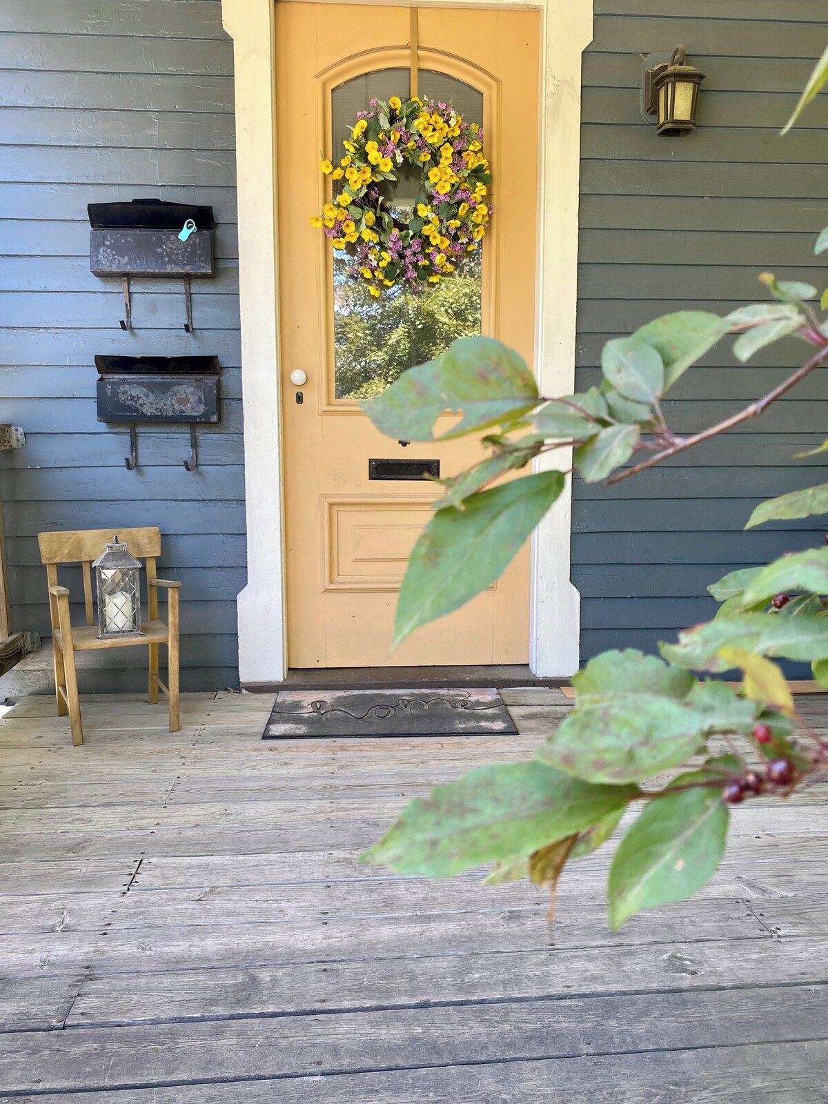 Une véranda en bois avec une porte, une boîte aux lettres et une petite chaise en bois.