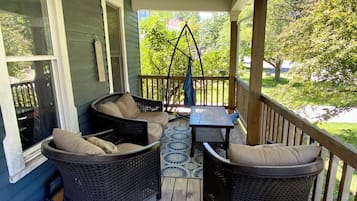 A covered porch with wicker furniture, a swing, and a view of a green landscape.