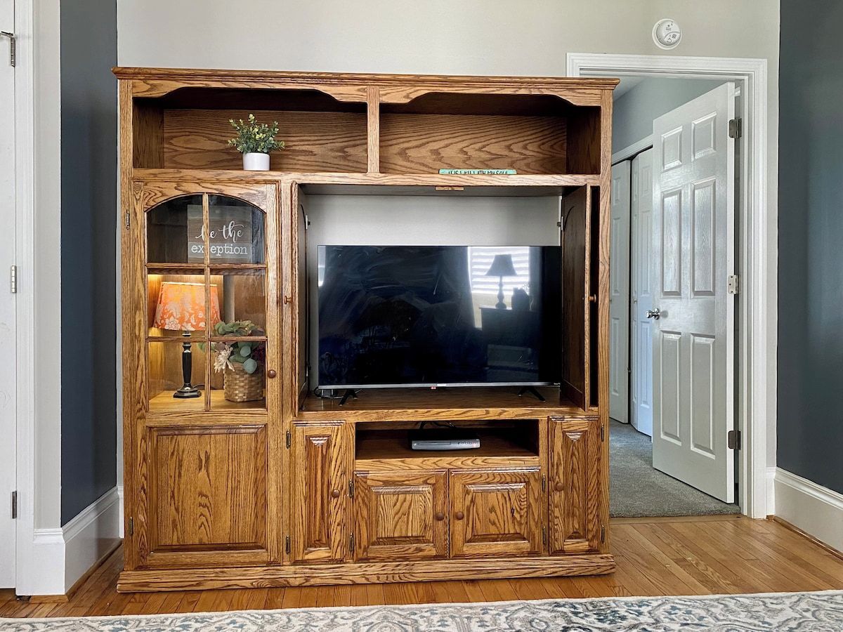 A wooden entertainment center with a television, a lamp, and decorative items.