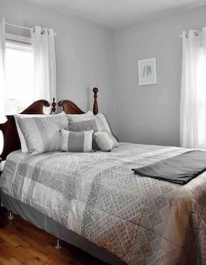 A bedroom with a wooden bed frame, patterned bedding, and a single framed picture on the wall. - Cozy Garden House (Adrian)