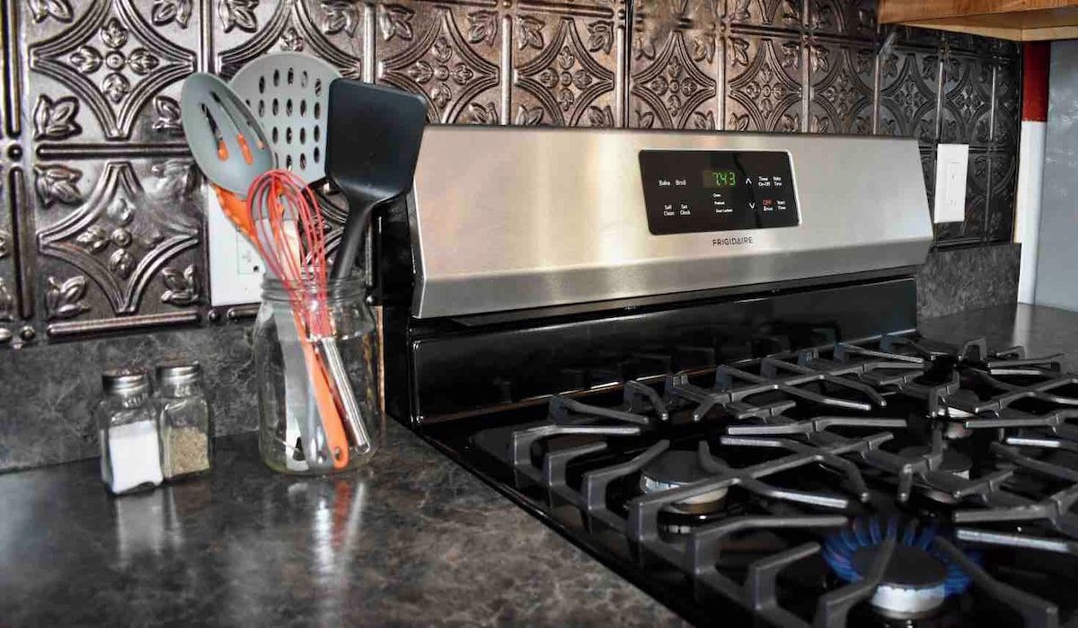 Una cocina con campana de acero inoxidable, pantalla digital y estufa a gas.
