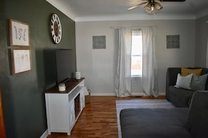A living room with a sofa, a television, a clock, and framed pictures on the wall. - Cozy Garden House (Adrian)