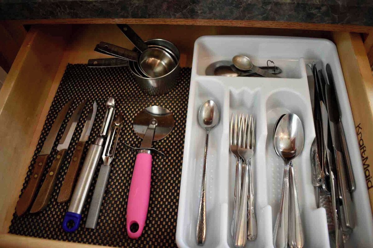 Uma gaveta com diversos utensílios de cozinha, incluindo facas, ralador e colheres medidoras.