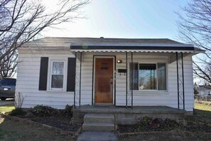 A single-story house with a front porch, a wooden door, and a small front yard. - Cozy Garden House (Adrian)