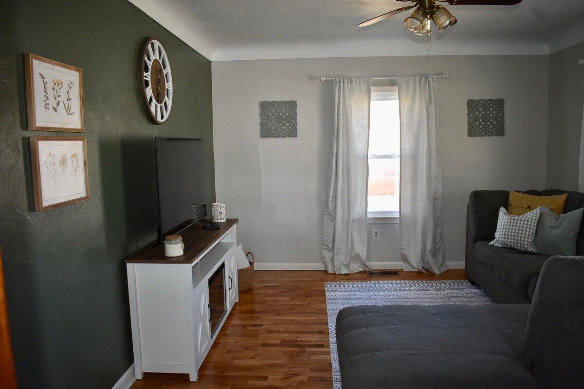 A living room with a sofa, a television, a clock, and framed pictures on the wall.