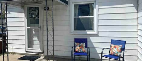 A house with a porch, two chairs with floral cushions, a window, and a door.