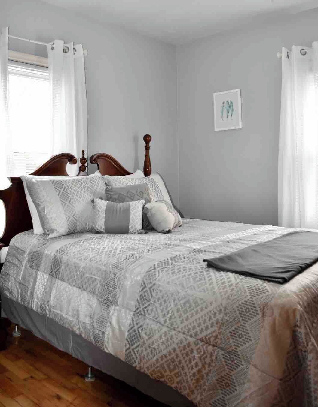 A bedroom with a bed, curtains, a headboard, a bedside table, and a wall-mounted picture.