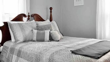 Une chambre à coucher avec un lit, des rideaux, une tête de lit, une table de chevet et un tableau accroché au mur.