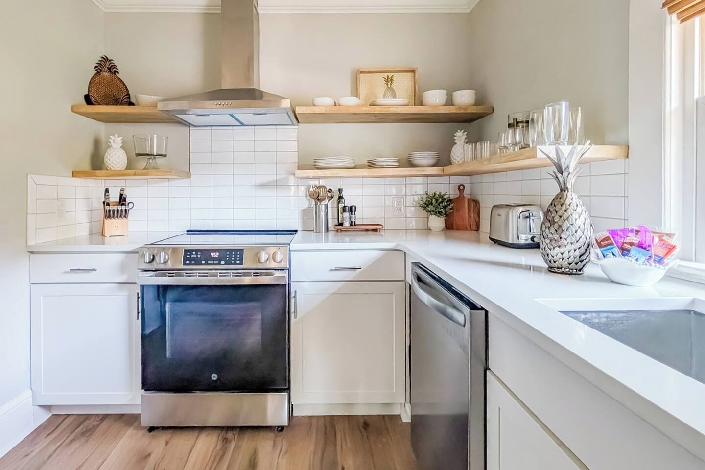 A modern kitchen with white cabinetry, stainless steel appliances, and wooden shelves.