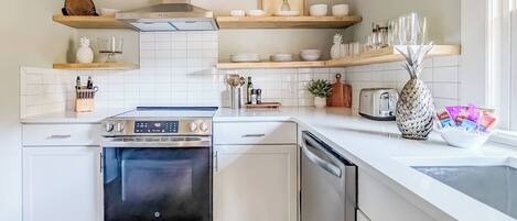 A modern kitchen with white cabinetry, stainless steel appliances, and wooden shelves.