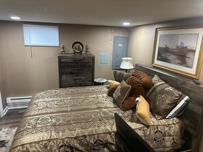 A bedroom with a large bed, a dresser, a lamp, and a painting on the wall.