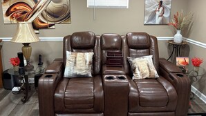 A massage chair in a room with artwork on the walls, a small table with a vase, and a glass table with electronic devices. - Cozy private one bedroom basement apartment with private parking and entrance. (Landover)