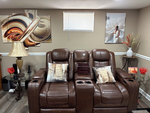 A massage chair in a room with artwork on the walls, a small table with a vase, and a glass table with electronic devices.