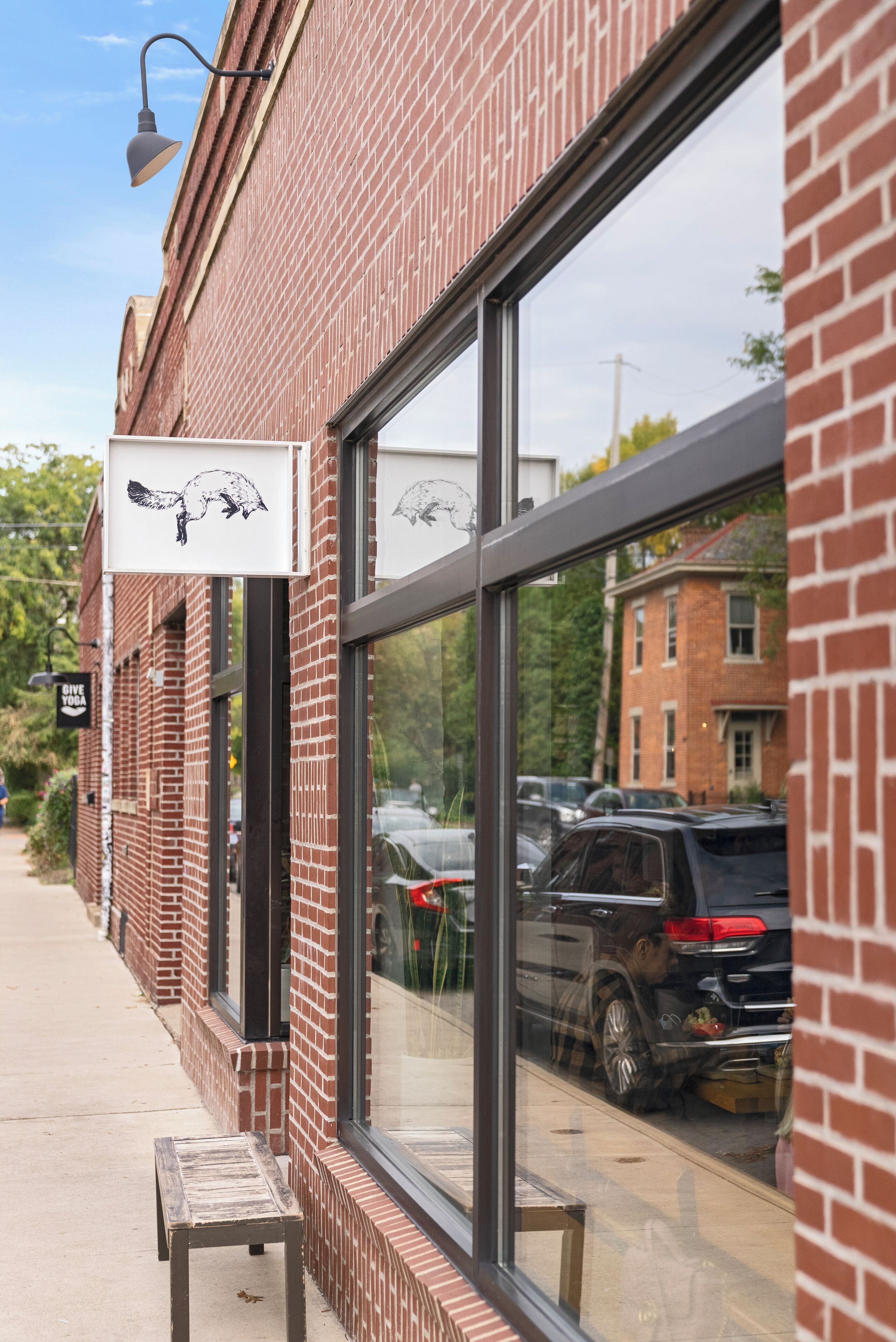 A brick building with large windows, a bench outside, and a car parked in front.