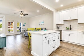 A modern kitchen with white cabinets, a central island, and a dining area with yellow chairs.