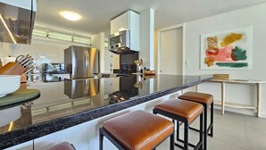 A modern kitchen with stainless steel appliances, a marble countertop, and a bar stool area.