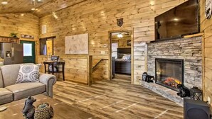 Un acogedor interior de cabaña de madera con chimenea, un sofá, un televisor y un comedor.