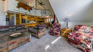 Ein geräumiges Loft mit hoher Decke, einem aufgehängten Stierkopf und einer gemütlichen Sitzecke mit gestreiften Sofas und einem Holztisch.