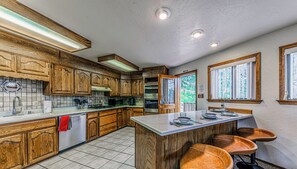 A kitchen with wooden cabinets, a central island with stools, and a view of the outdoors through a window.
