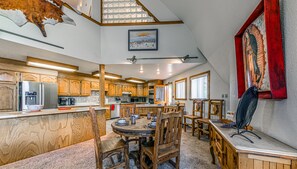 A spacious kitchen with wooden cabinets, a dining area with a round table and chairs, and a large painting on the wall.