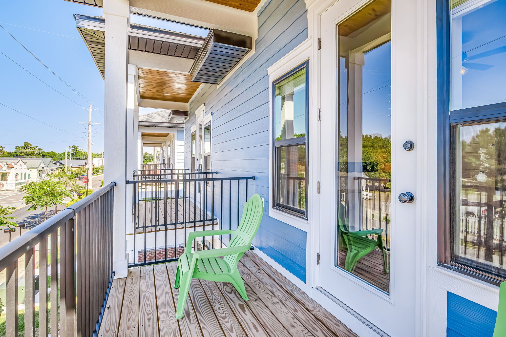 A covered porch with a green chair, a railing, and a view of the street.
