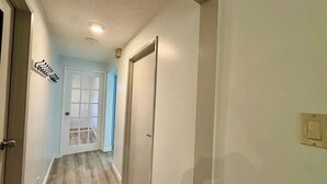 Un corridoio con pavimento in legno, una porta bianca e un interruttore sulla parete.
