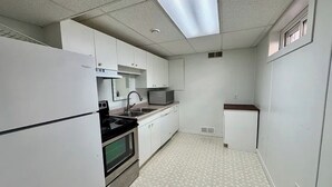 Una cucina compatta con mobili bianchi, un forno a microonde, un fornello e un frigorifero.