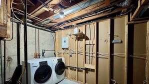 Una lavanderia con due lavatrici, cablaggi elettrici a vista e pareti non rifinite.