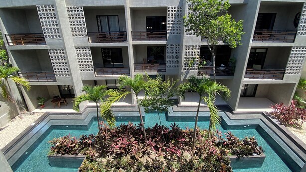 A modern multi-story building with balconies, a swimming pool, and surrounding greenery. - Casa Frida Kahlo (Tulum)