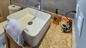 A bathroom with a white sink, a round mirror, wooden shelves with towels, a toilet, and a coffee machine. - Casa Frida Kahlo (Tulum)