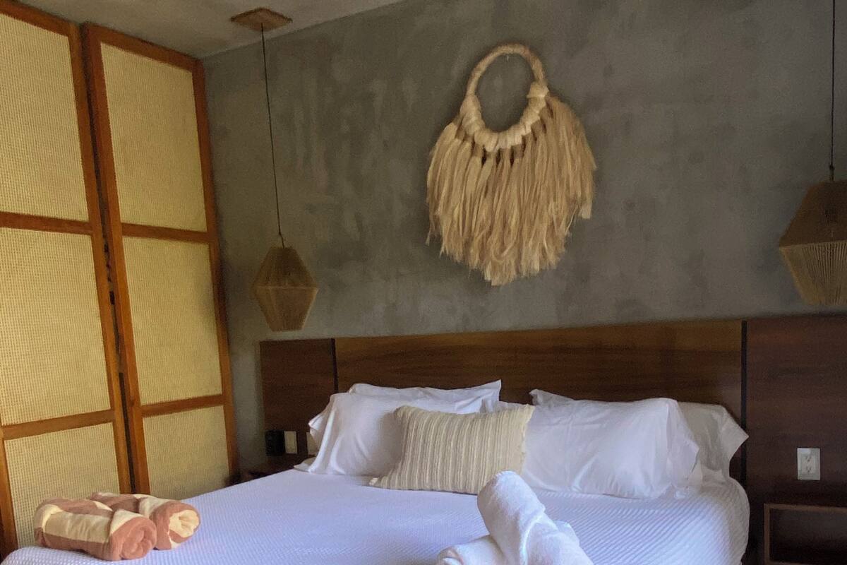 A bed with a white textured bedspread, a wooden headboard, and a woven macrame wall hanging.