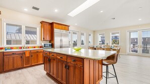 A spacious kitchen with wooden cabinets, a large island, and a view of the neighborhood through large windows.