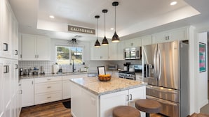 A modern kitchen with white cabinets, a stainless steel refrigerator, and a central island with stools.