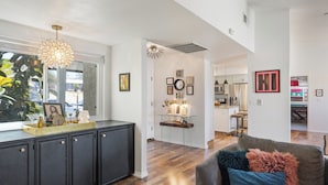 A modern kitchen with a dining area, wooden flooring, and a view through a window.