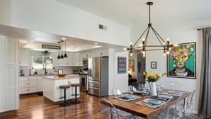 A modern kitchen with white cabinets, stainless steel appliances, and a wooden dining table set for six.