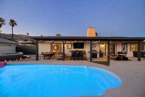 A backyard with a swimming pool, outdoor dining area, barbecue grill, and a covered patio.