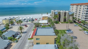 A coastal hotel with a beach view, multiple parking areas, and a central courtyard with palm trees. - 🐚Seashell Oasis B-1 - Beautiful Condo steps to the Beach! (Redington Shores)
