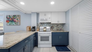 A compact kitchen with white appliances, dark cabinets, and a tiled backsplash. - 🐚Seashell Oasis B-1 - Beautiful Condo steps to the Beach! (Redington Shores)