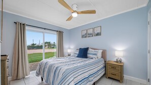A bedroom with a bed, nightstands, a ceiling fan, and a view of the outdoors. - 🐚Seashell Oasis B-1 - Beautiful Condo steps to the Beach! (Redington Shores)