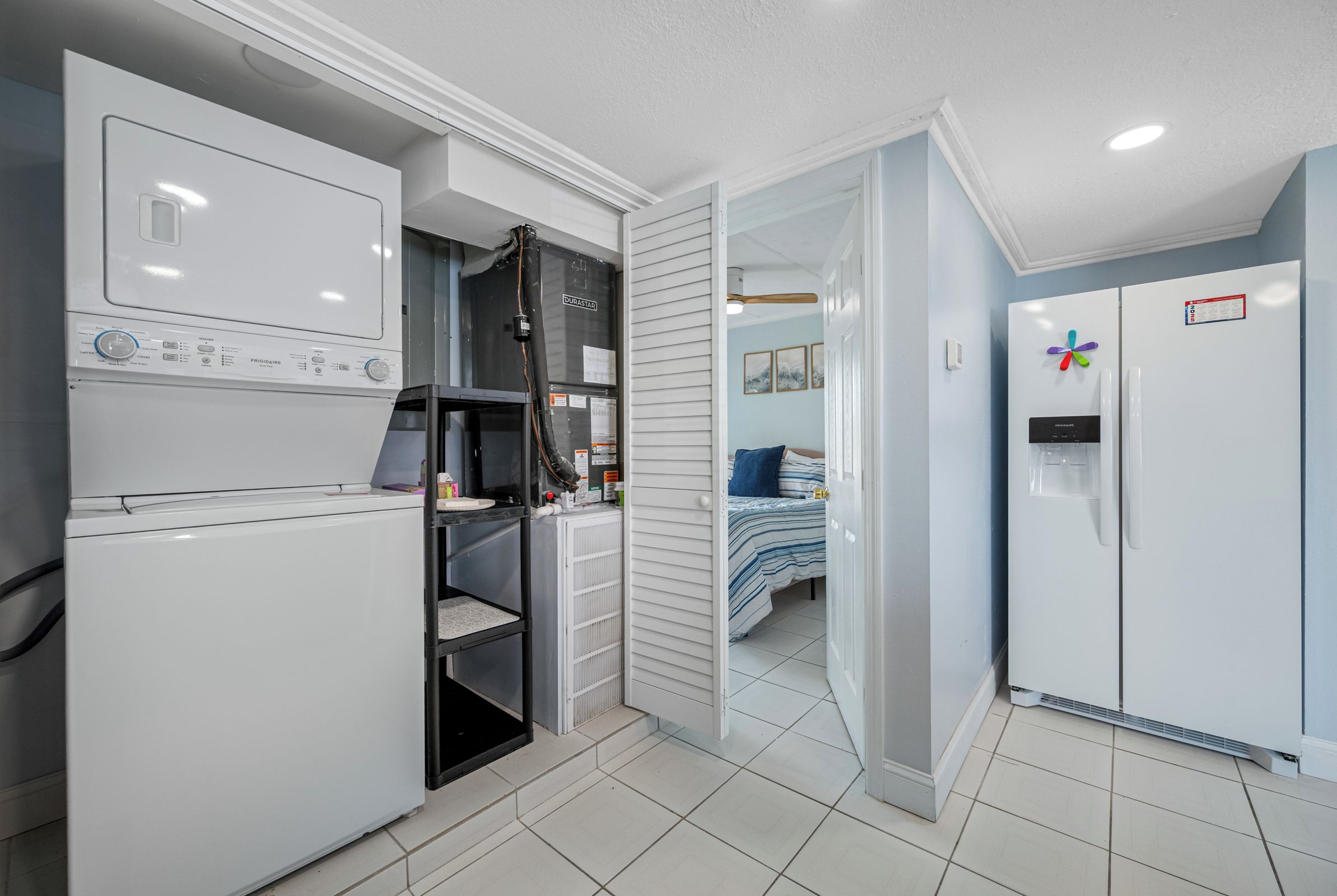A compact kitchen with a washing machine, a refrigerator, and a bed in the adjacent room.
