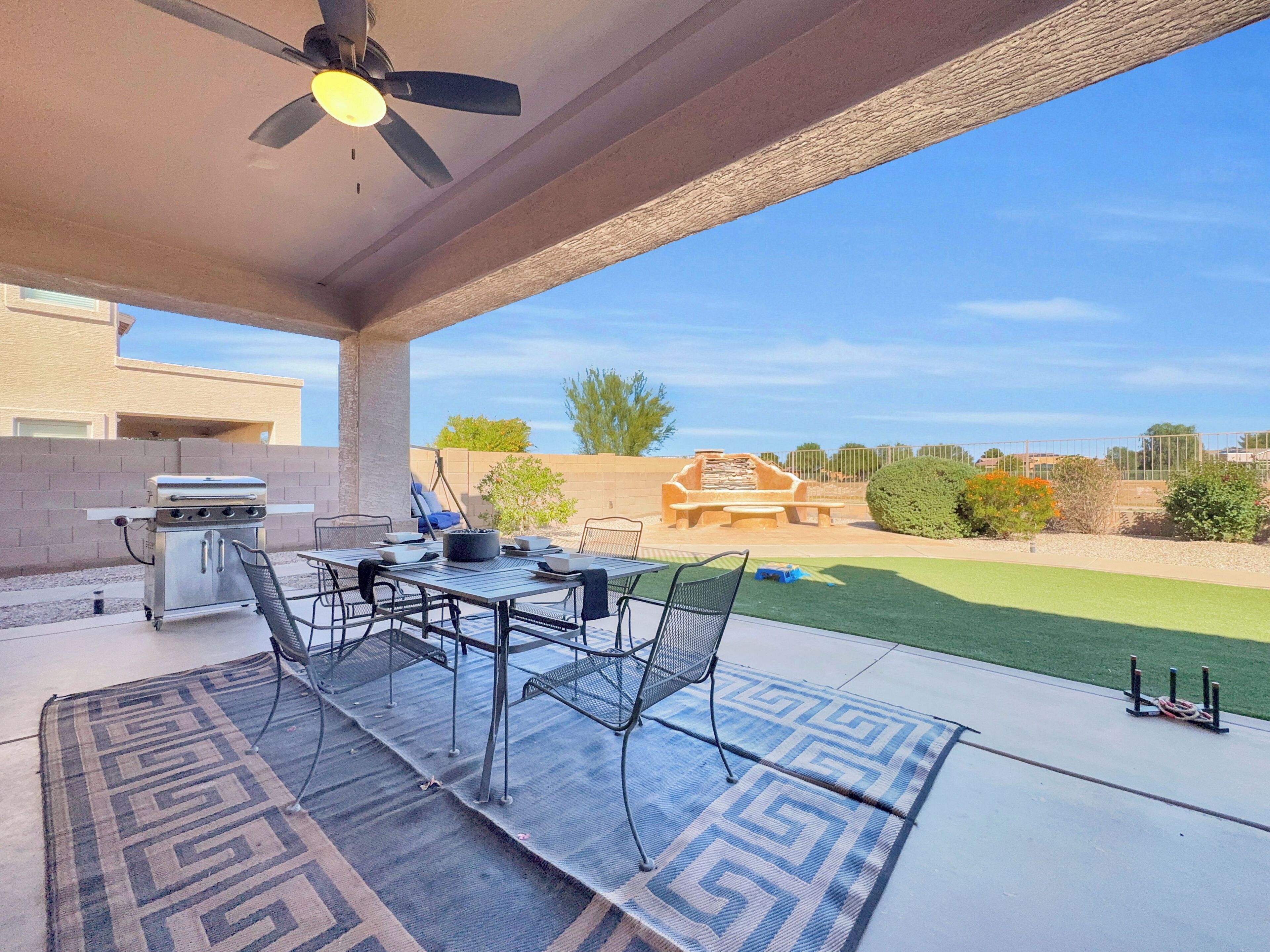 Une terrasse extérieure équipée d’un barbecue, d’une table à manger, de chaises et d’un ventilateur de plafond.