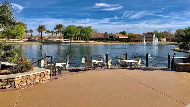 Une terrasse au bord du lac, avec des tables et des chaises, un mur en pierre et une fontaine en arrière-plan.