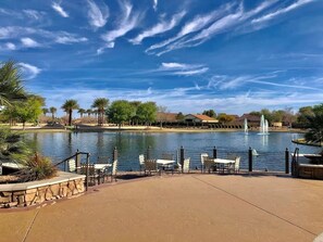 Une terrasse au bord du lac, avec des tables et des chaises, un mur en pierre et une fontaine en arrière-plan.