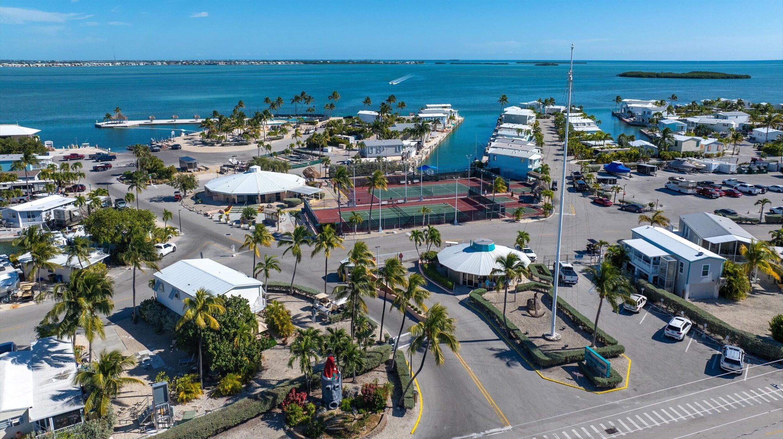 Una zona costera con un puerto deportivo, varios edificios y una cancha de tenis.