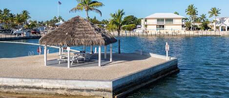 A beachside pier with a thatched-roof gazebo, picnic tables, and a lifebuoy.